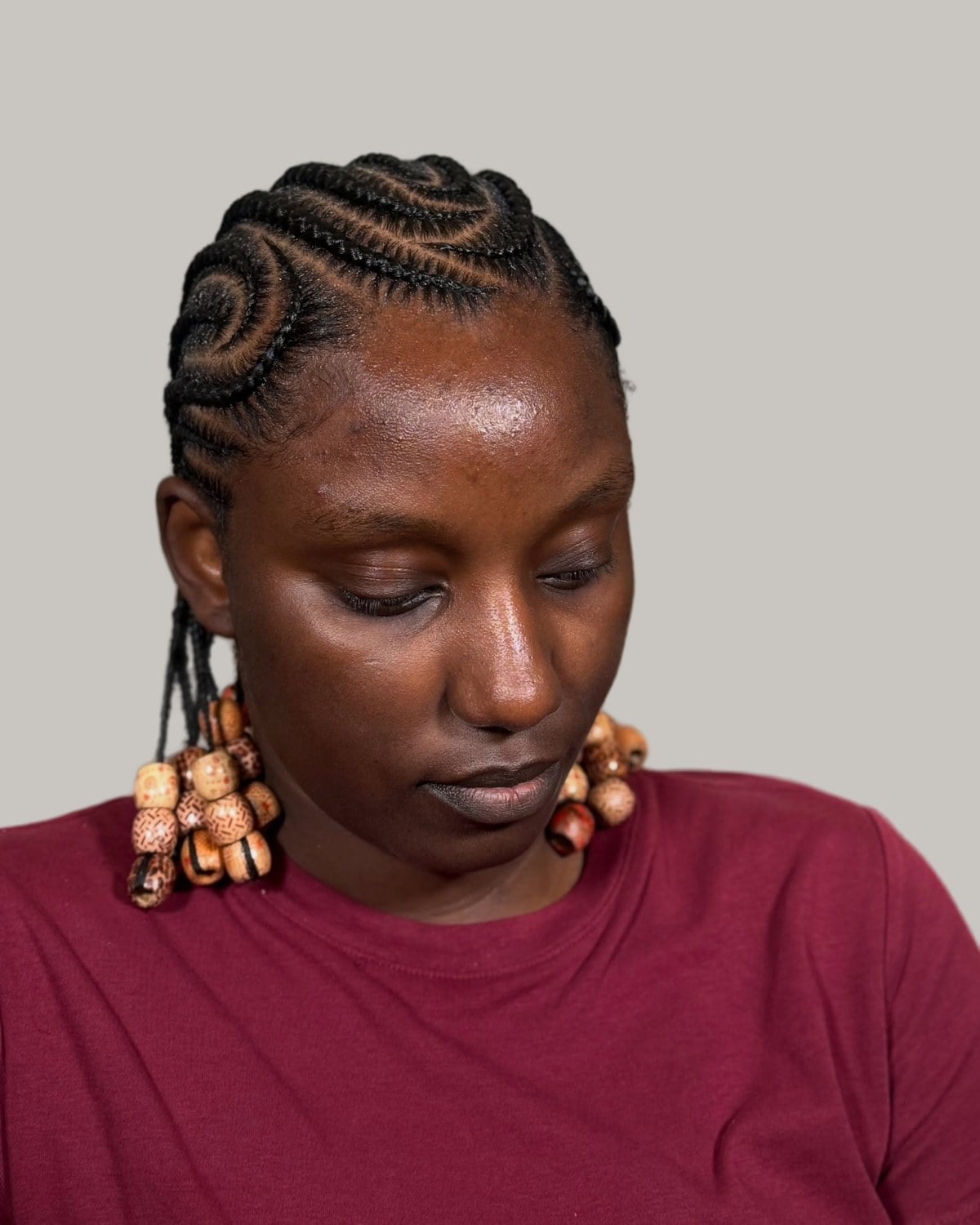 Woman in a burgundy top with short Fulani braids and stacked wooden beads