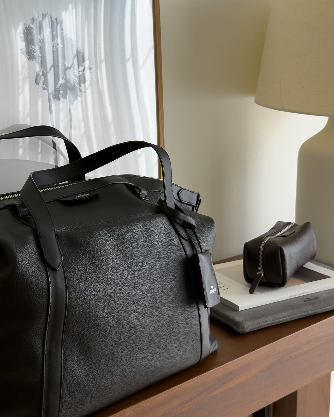 Harber London Leather Overnight Bag on a side table next to a leather dopp kit and a lamp - Luxe Digital
