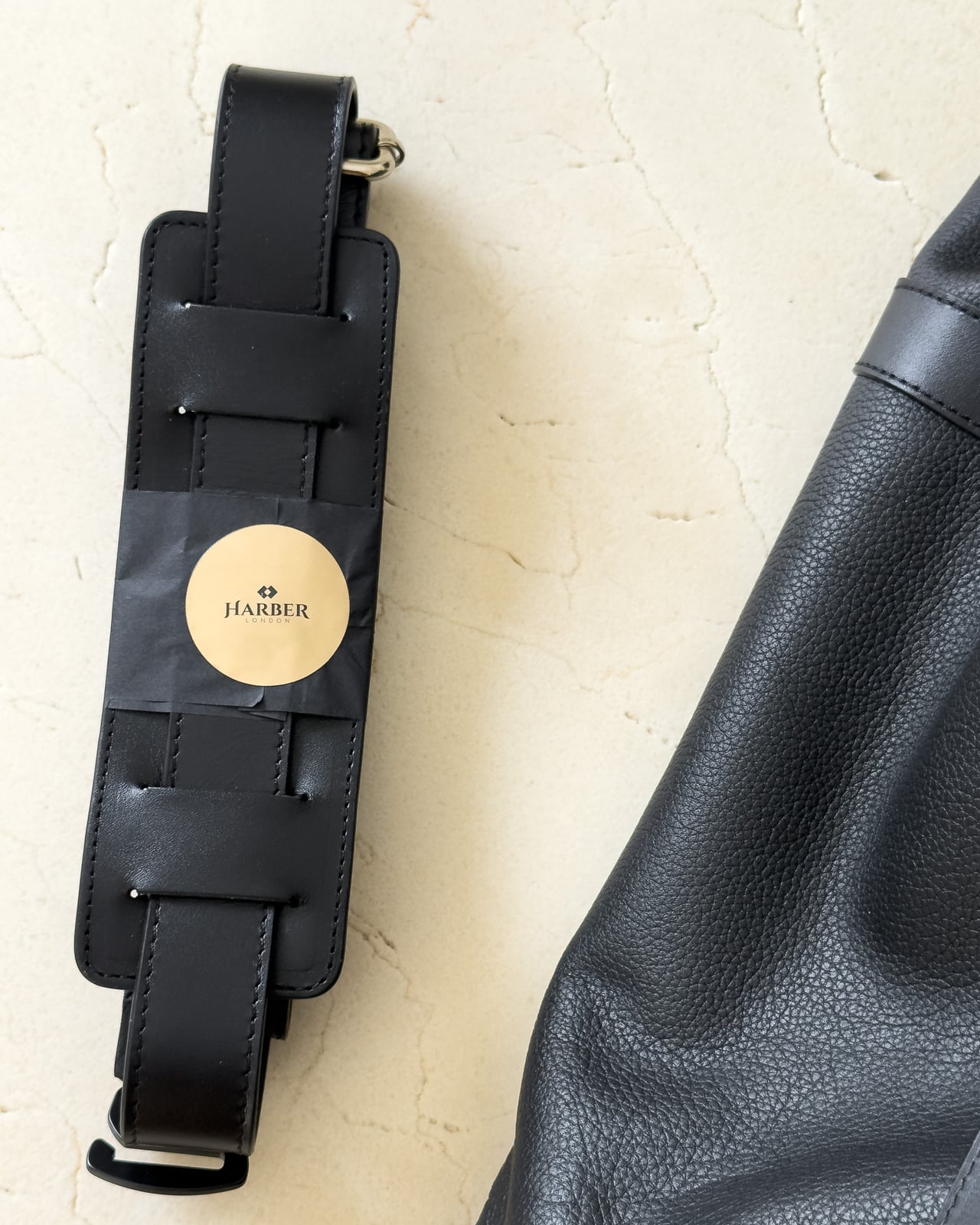 Harber London detachable leather shoulder strap still wrapped with a gold Harber London sticker beside the bag - Luxe Digital