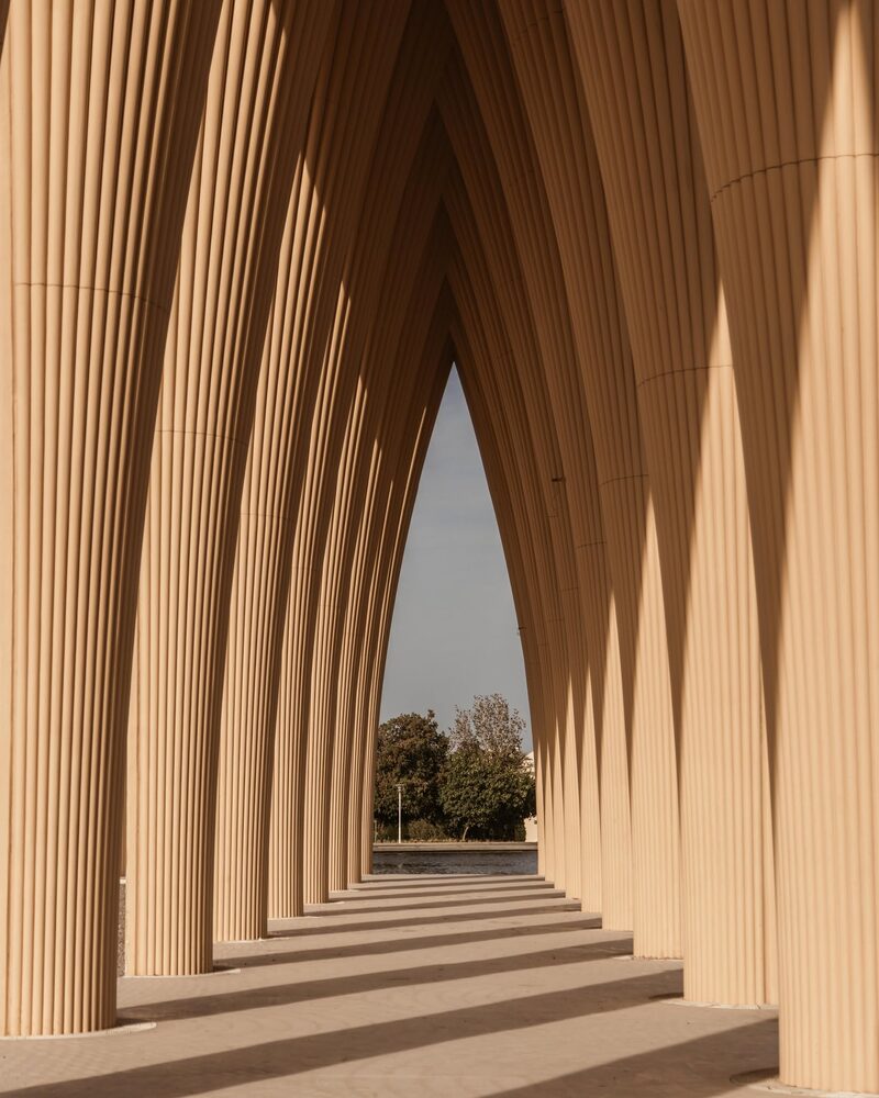 A sculptural colonnade of pale arches framing a view of trees and water