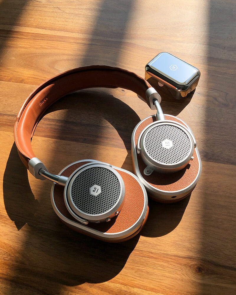 Leather-trimmed over-ear headphones and a smartwatch on a sunlit wooden desk