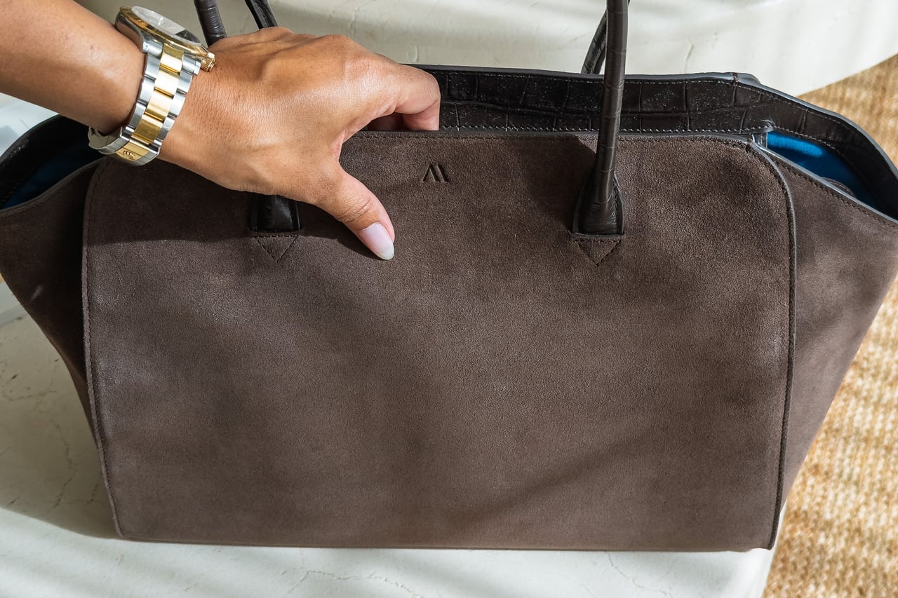 Hand resting on the suede side of the KAAI Voyager beside its discreet logo - Luxe Digital