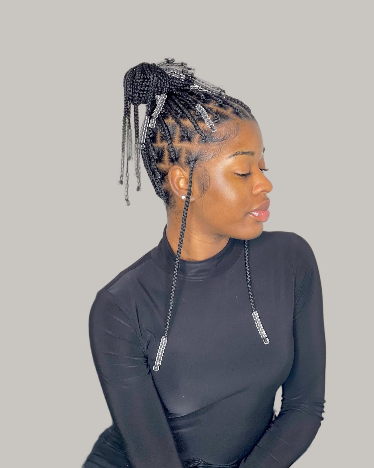 Woman in a black top in profile with knotless braids pulled into a high bun