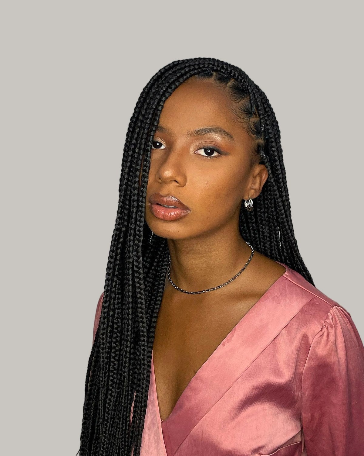 Woman in a pink satin blouse in three-quarter view with long black medium knotless braids