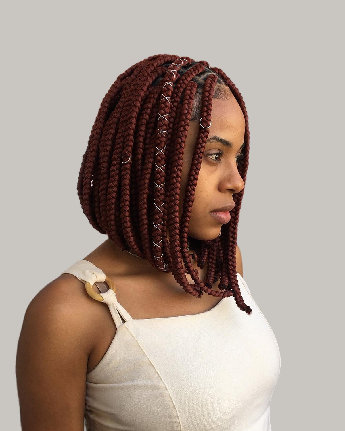 Woman in a cream top in profile with an auburn knotless braid bob