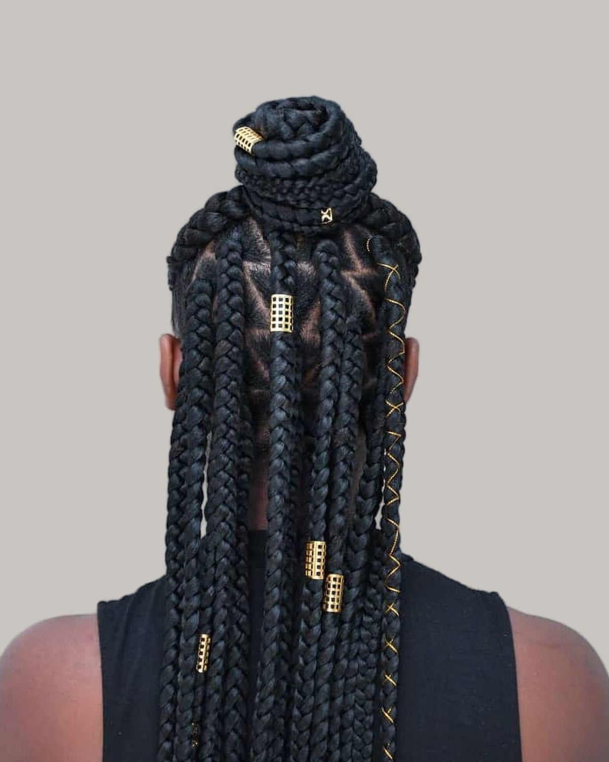 Back view of black large knotless braids, the top half in a bun and the rest down, with gold cuffs