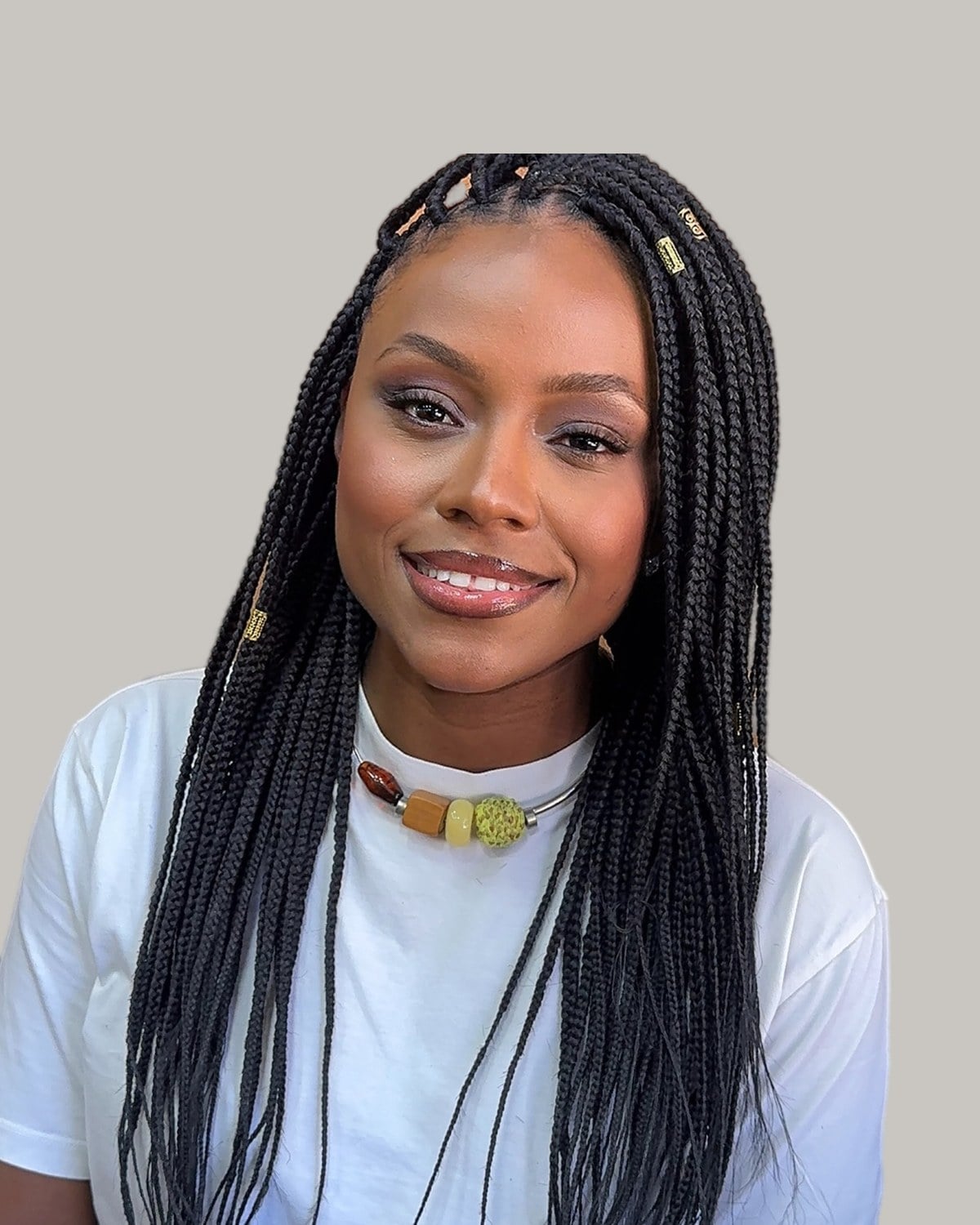 Smiling woman in a white T-shirt and beaded necklace with black knotless box braids