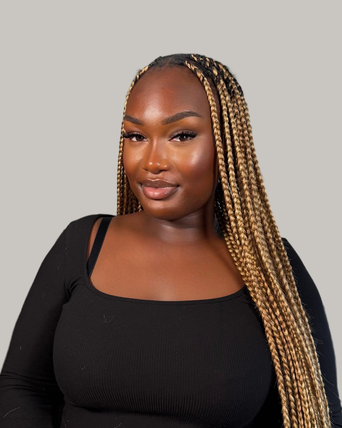 Smiling woman in a black top with large honey-blonde and brown knotless braids swept to one side