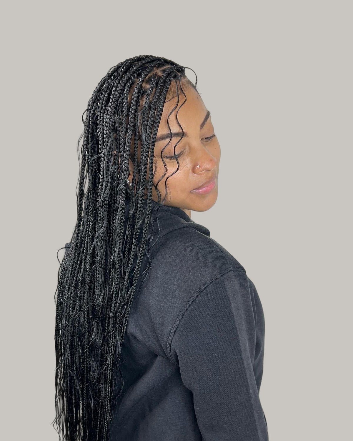 Woman in a black hoodie in three-quarter view, black mini knotless braids with wavy pieces