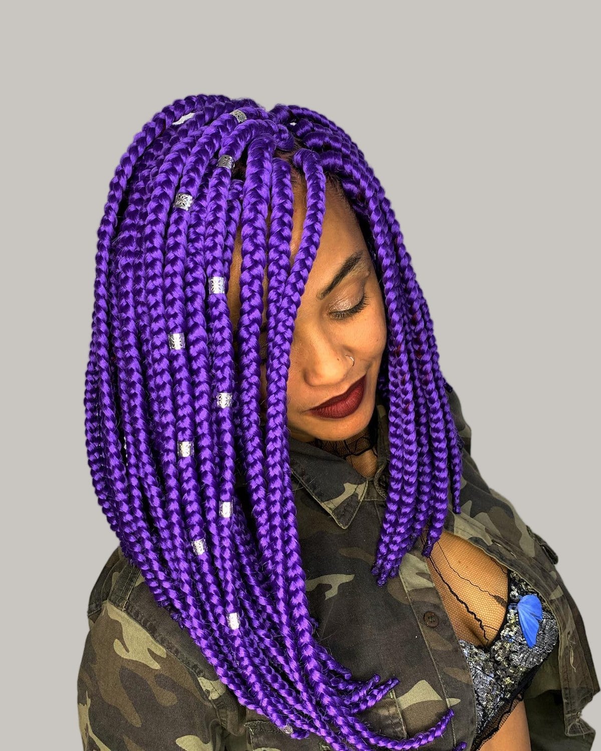 Woman in a camouflage jacket with a purple knotless braid bob and silver cuffs