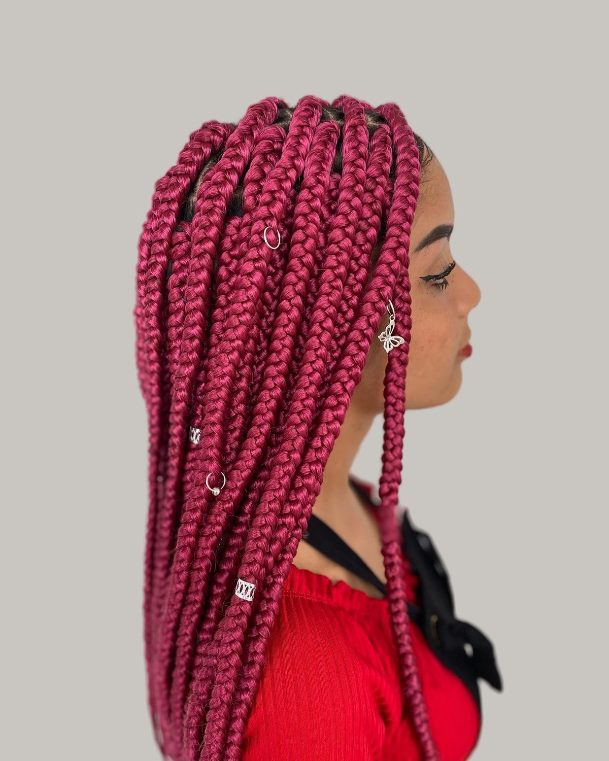Woman in a red top in profile with raspberry-red large knotless braids