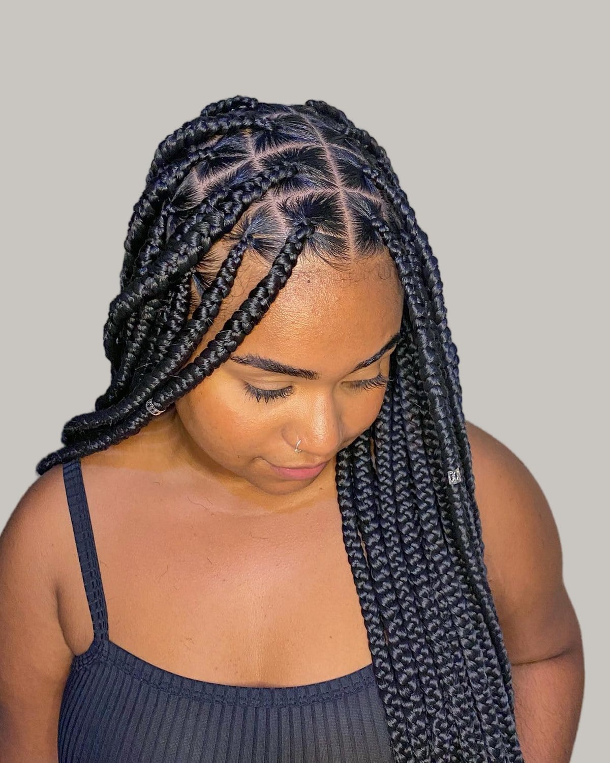 Woman in a black tank top looking down, black scant knotless braids with triangle parts