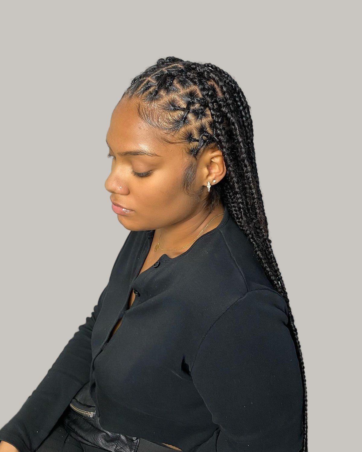 Woman in a black cardigan in profile, looking down, black knotless braids with triangle parts