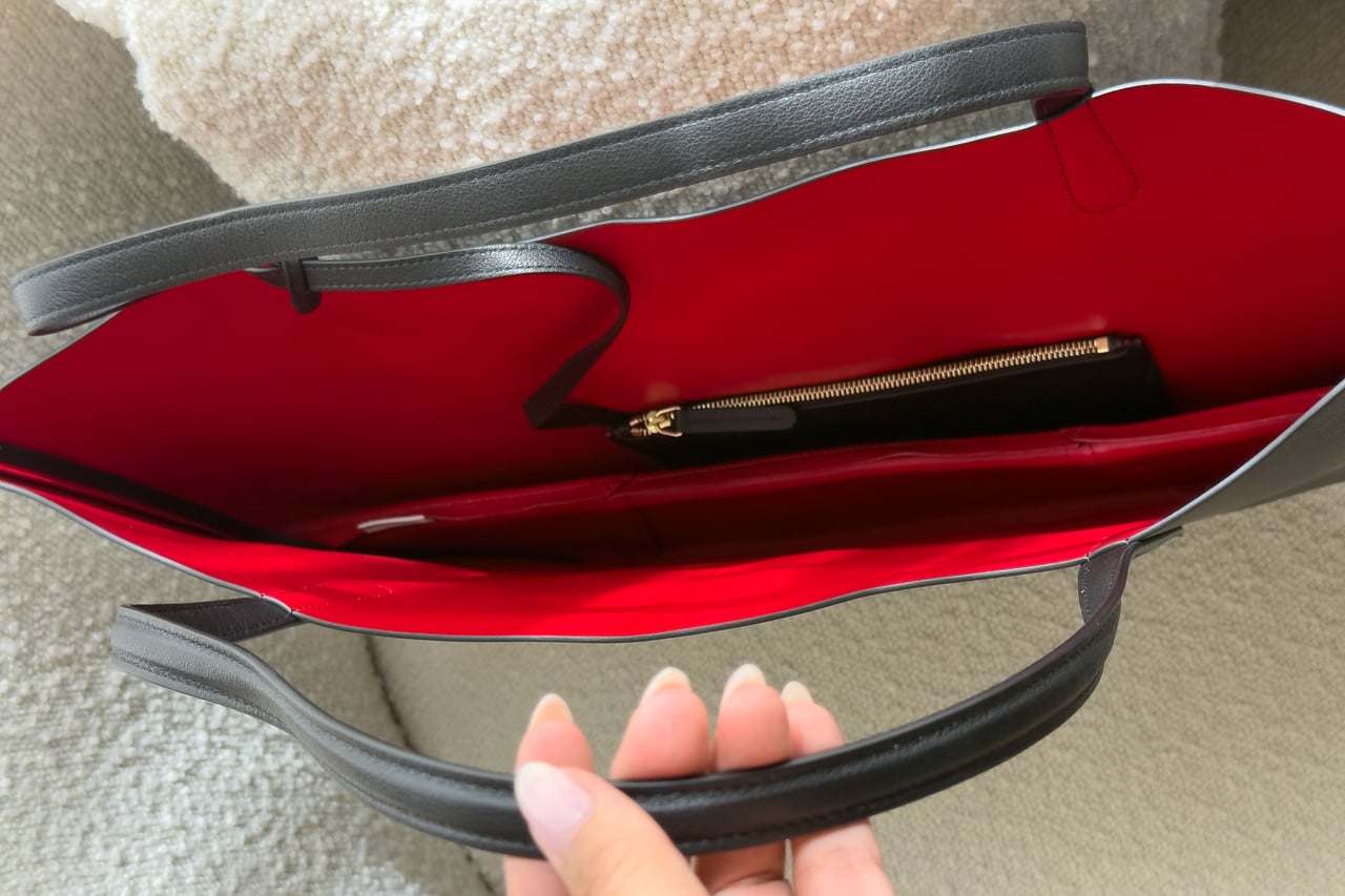 Hand holding the two long black handles above the red interior and its zipped pocket - Luxe Digital