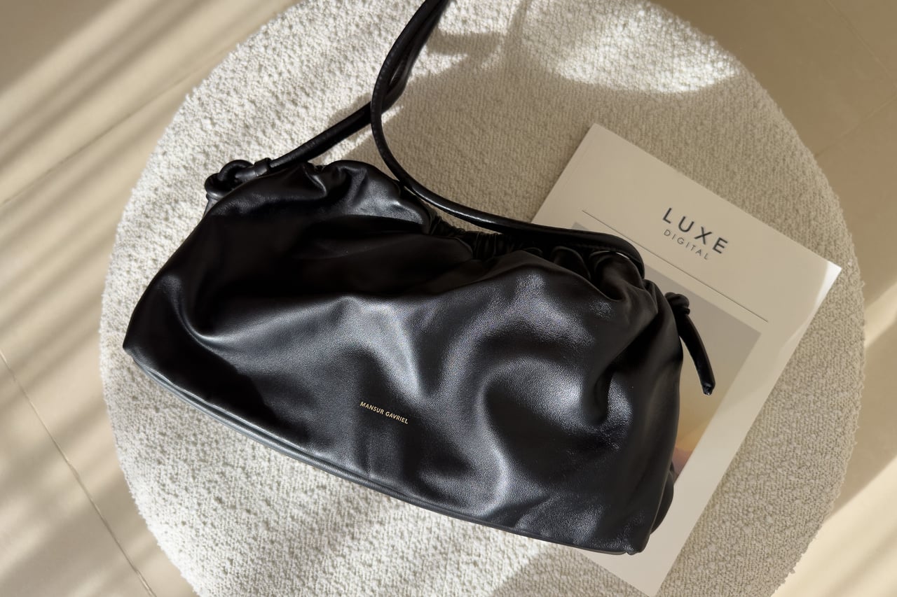 Black Mansur Gavriel Oversized Cloud with its shoulder strap on a round stool - Luxe Digital