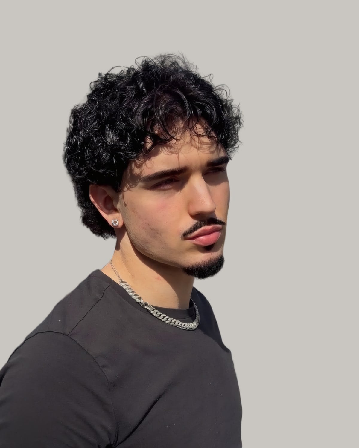 Man with big dark curls, a curly fringe and a goatee, seen at an angle