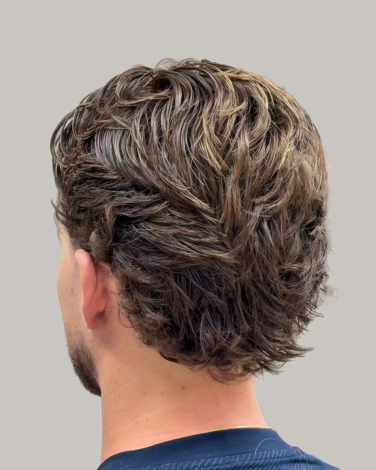 Man with textured light-brown waves pushed up, seen from behind at an angle