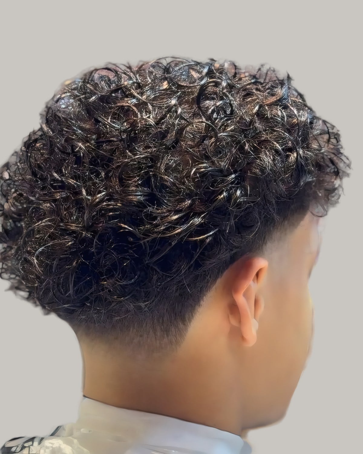 Man with a curly top and a fade, seen from behind
