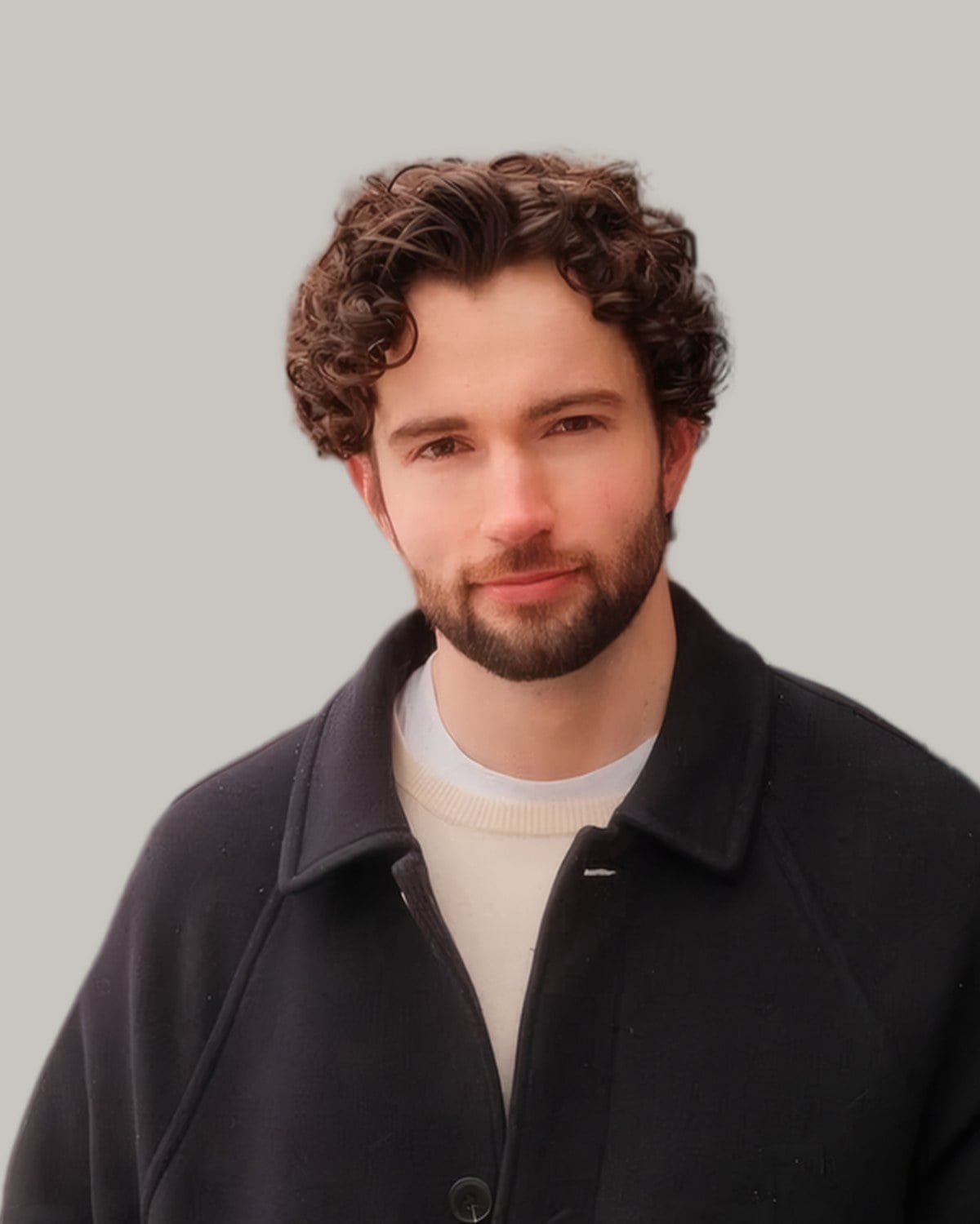 Bearded man with a curly top pushed up and back, in a dark coat, seen from the front