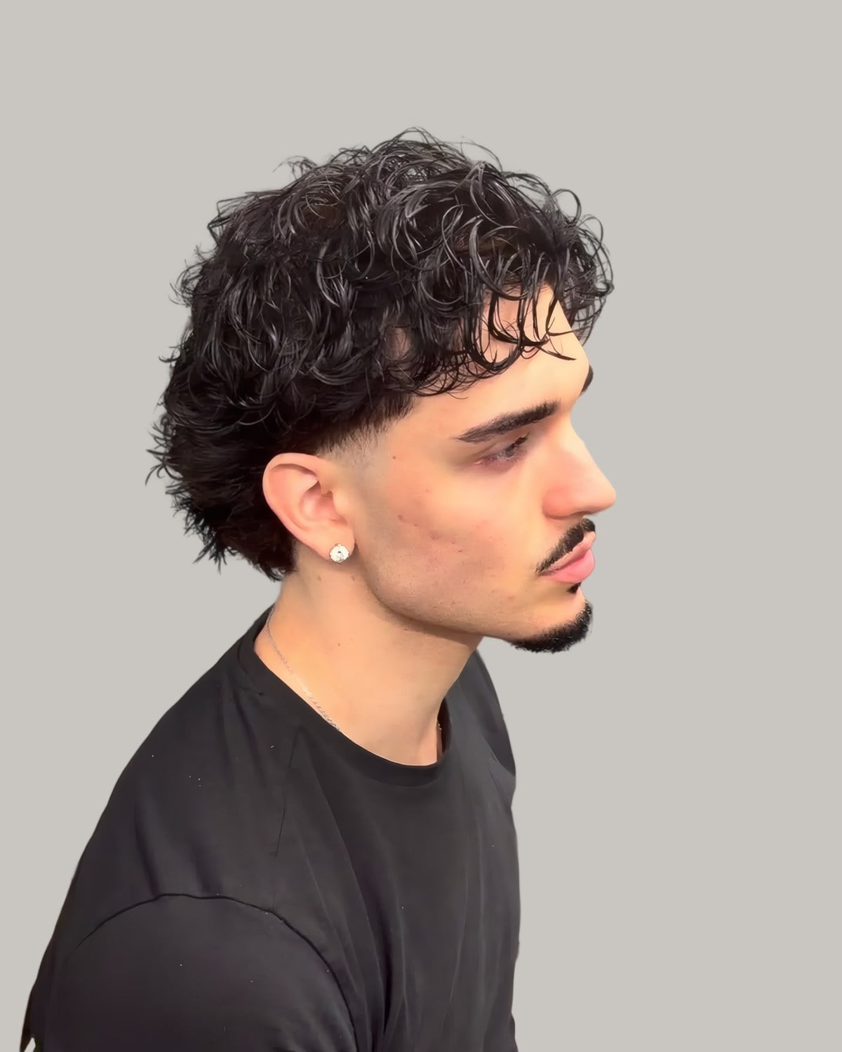 Man with a damp curly mullet, a fringe and a low taper, seen in profile