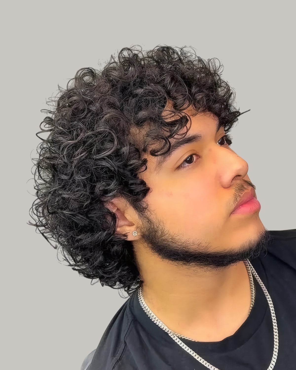 Man with thick curls and a beard, seen in profile looking up