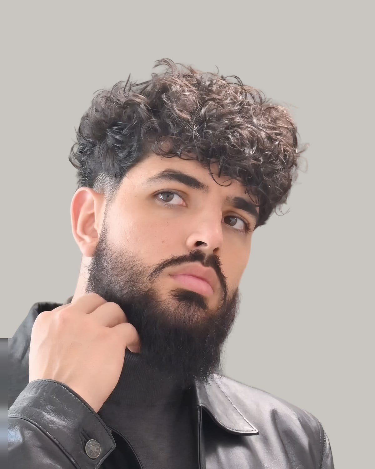 Bearded man with a curly top and a fade, holding his beard, seen from the front