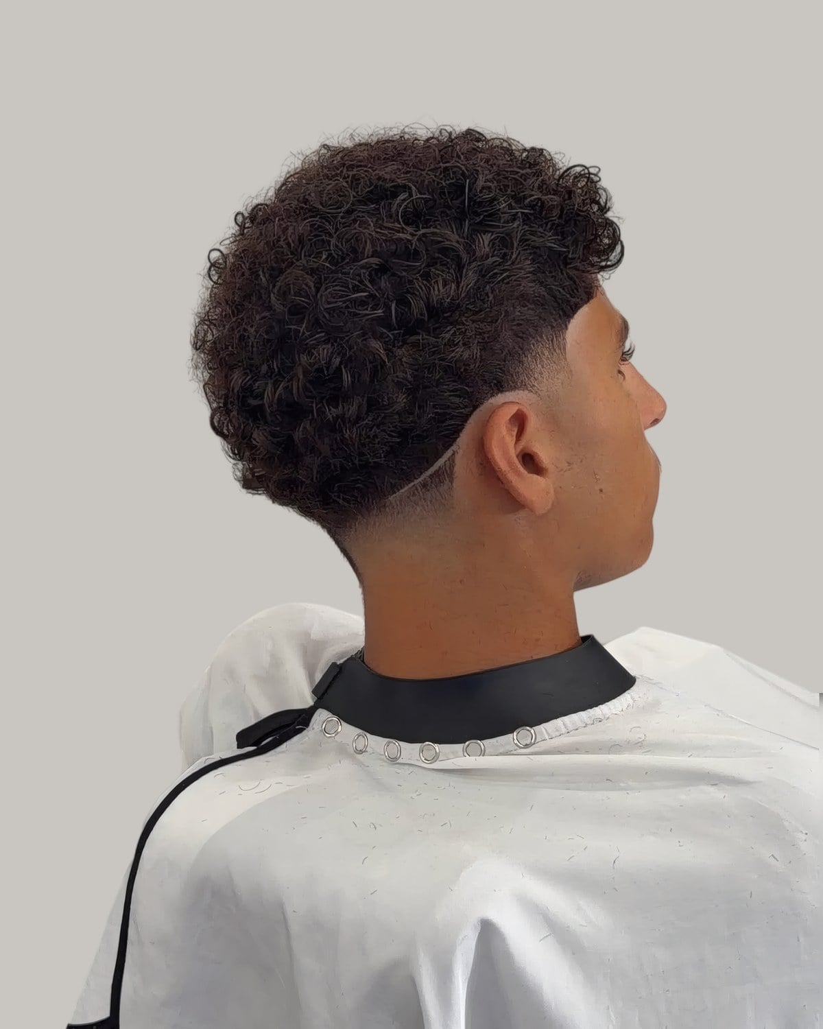 Man with a round curly top and a skin fade, seen from behind at an angle