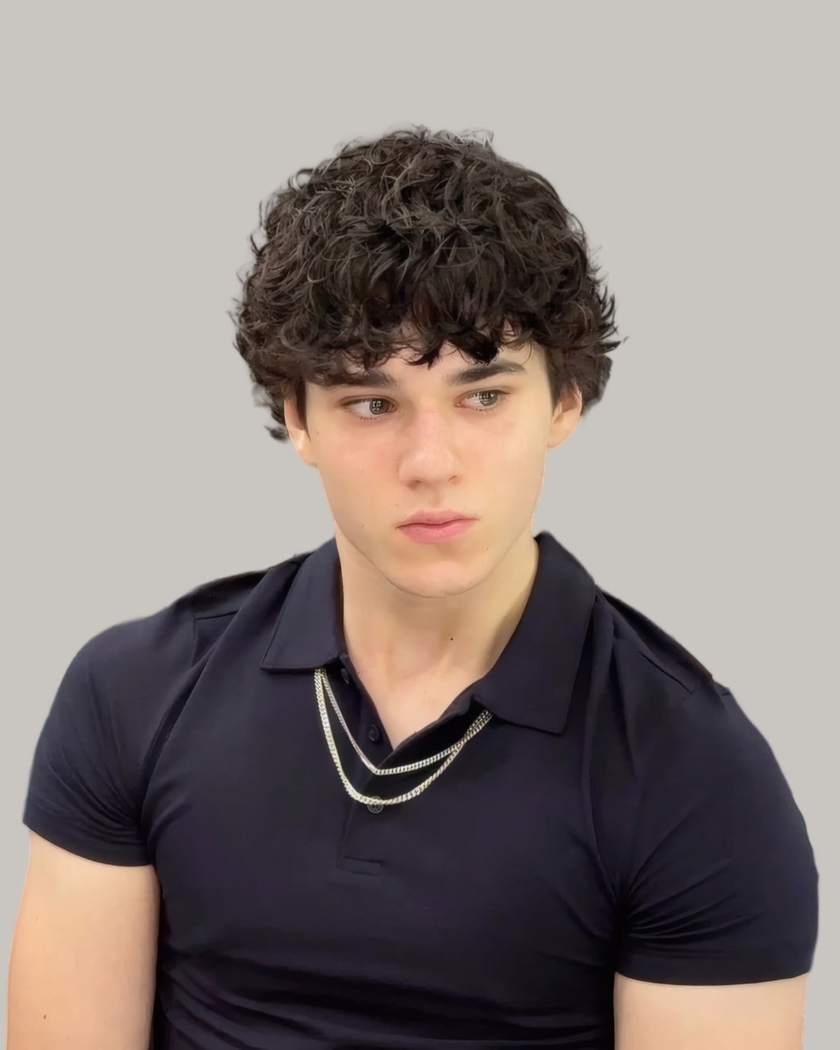 Man with a full top of dark curls falling into a short fringe, in a navy polo