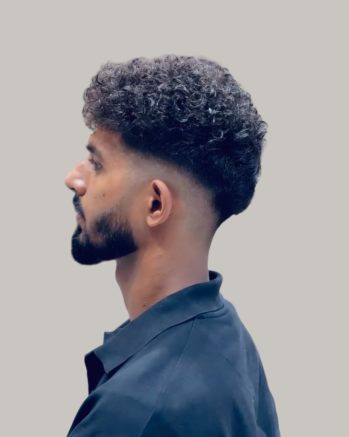 Bearded man with a curly top and a fade, seen in profile