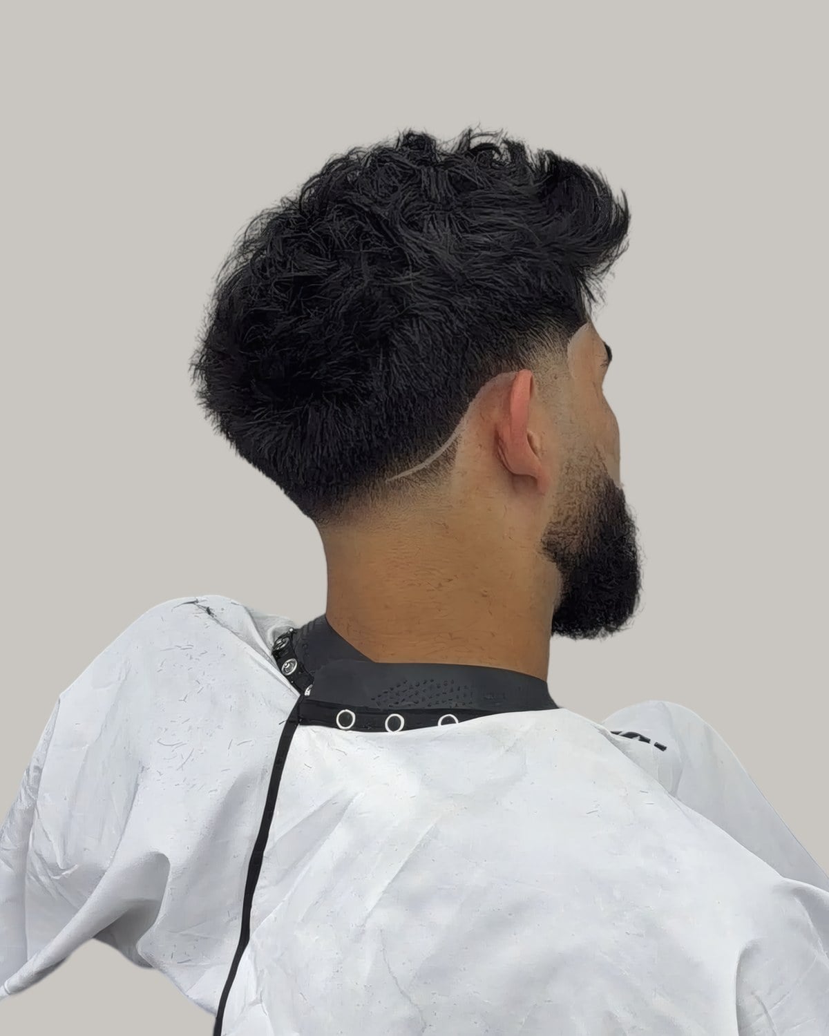 Man with a curly top and a low fade, seen from behind at an angle