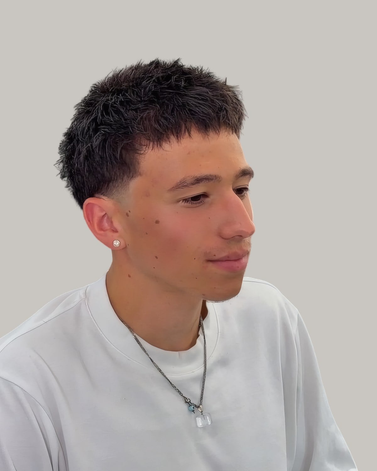 Young man with dense short curls and a taper, seen from the front at an angle
