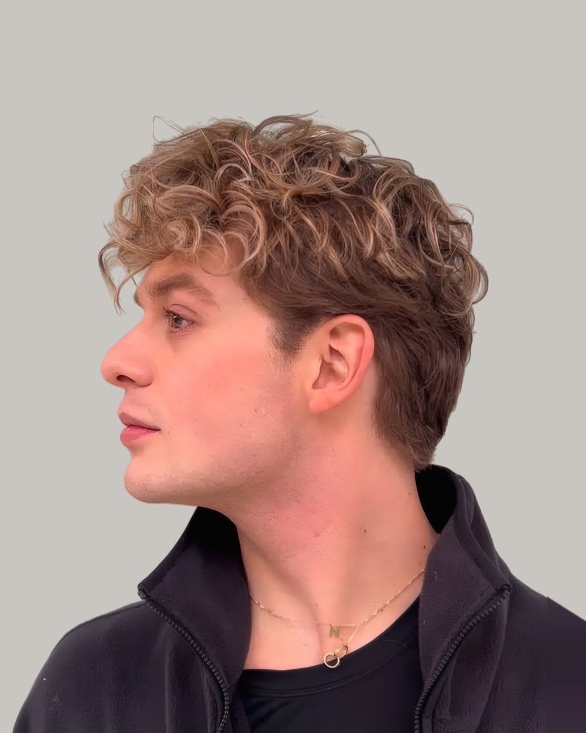 Young man with curly light brown hair lightened to blonde at the ends, seen in profile