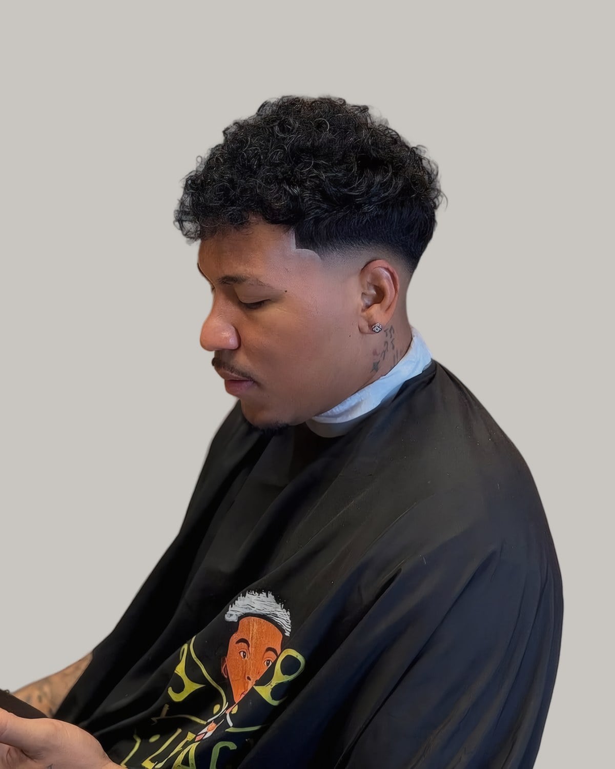 Man with a messy short curly top and a fade, seen from the side