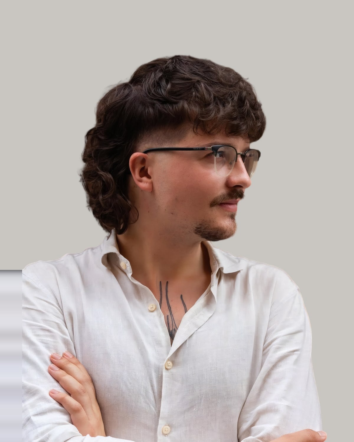 Man with glasses and a wavy dark mullet over a taper at the temple, arms crossed