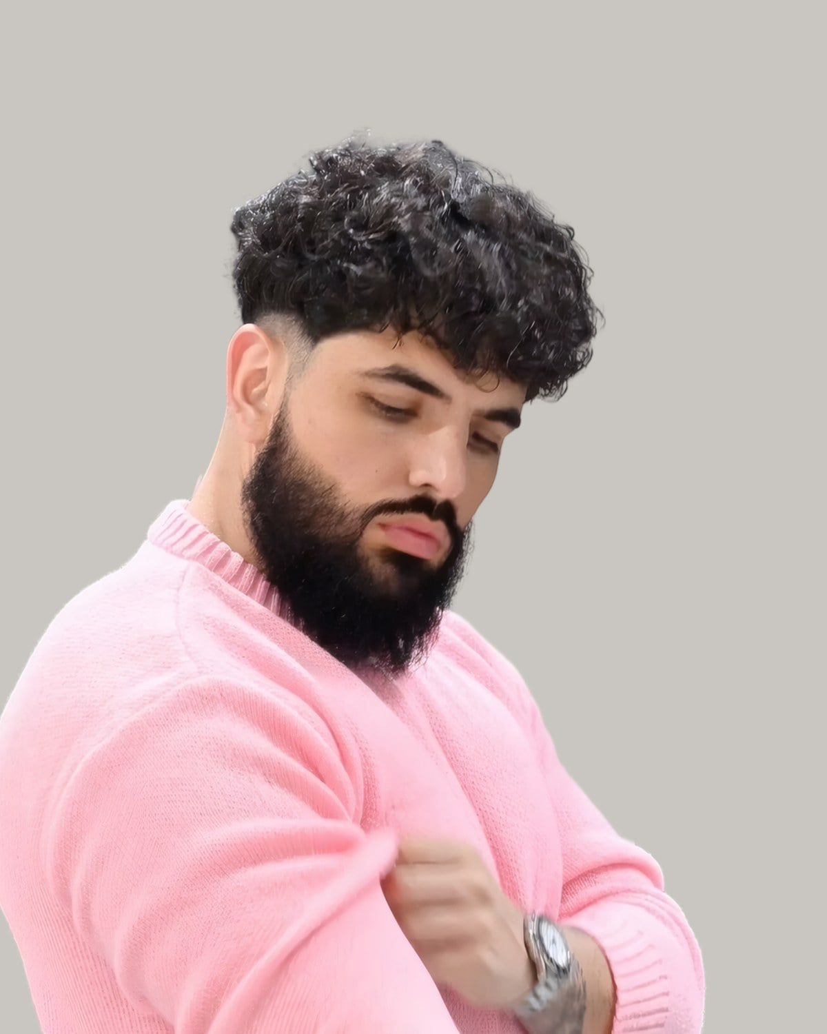 Bearded man with a curly fringe and a skin fade at the temple, in a pink sweater, looking down