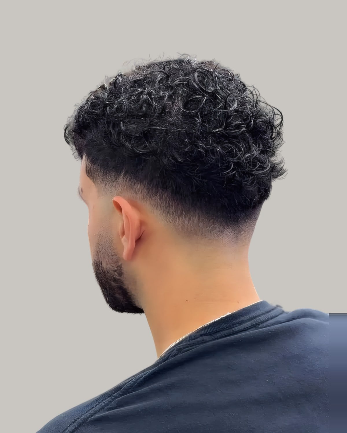 Man with curls on top and a mid fade, seen from behind at an angle