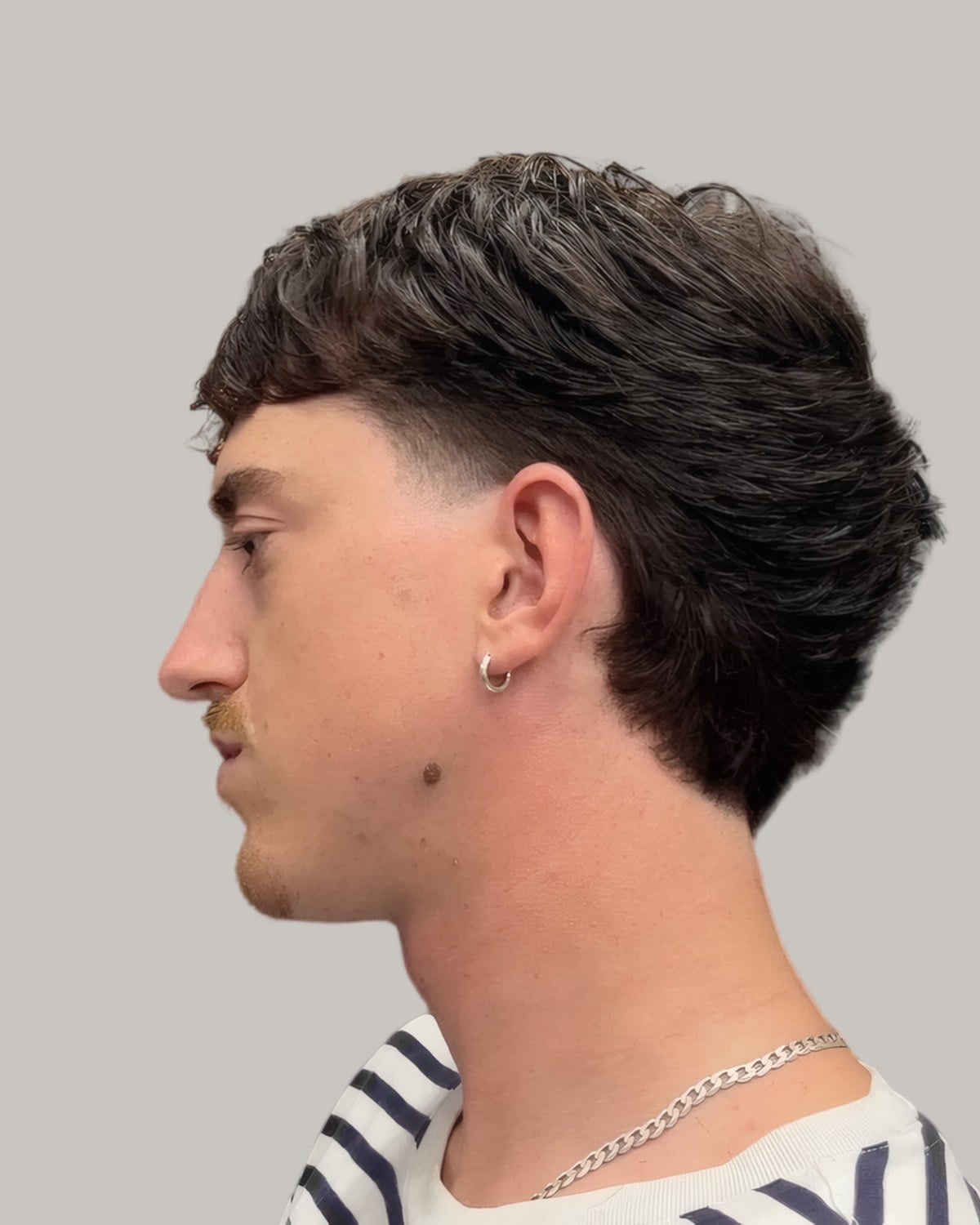 Young man with a dark textured fringe falling forward and tapered sides, seen in profile