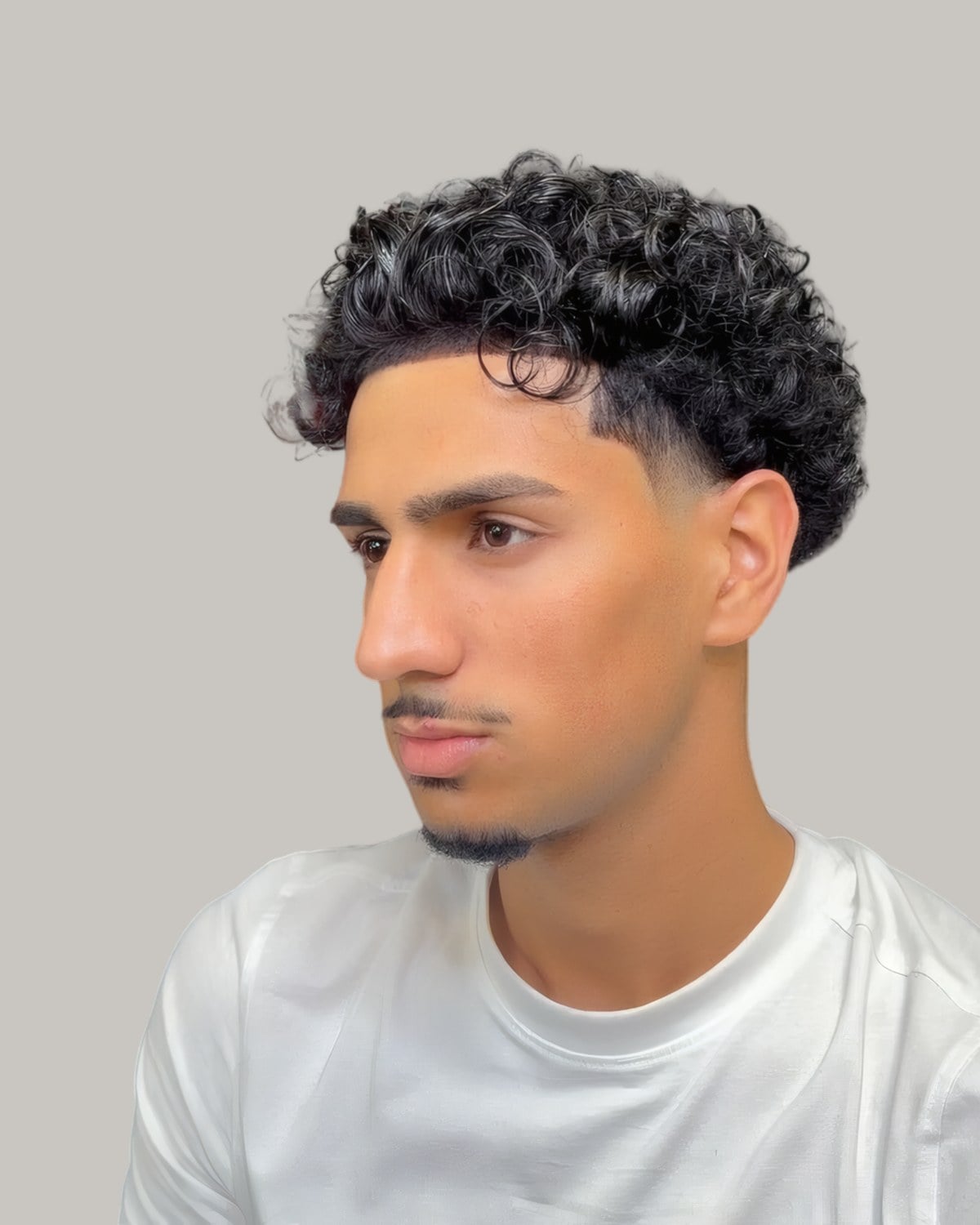 Man with dark curls on top and a fade at the sides, seen from the front at an angle