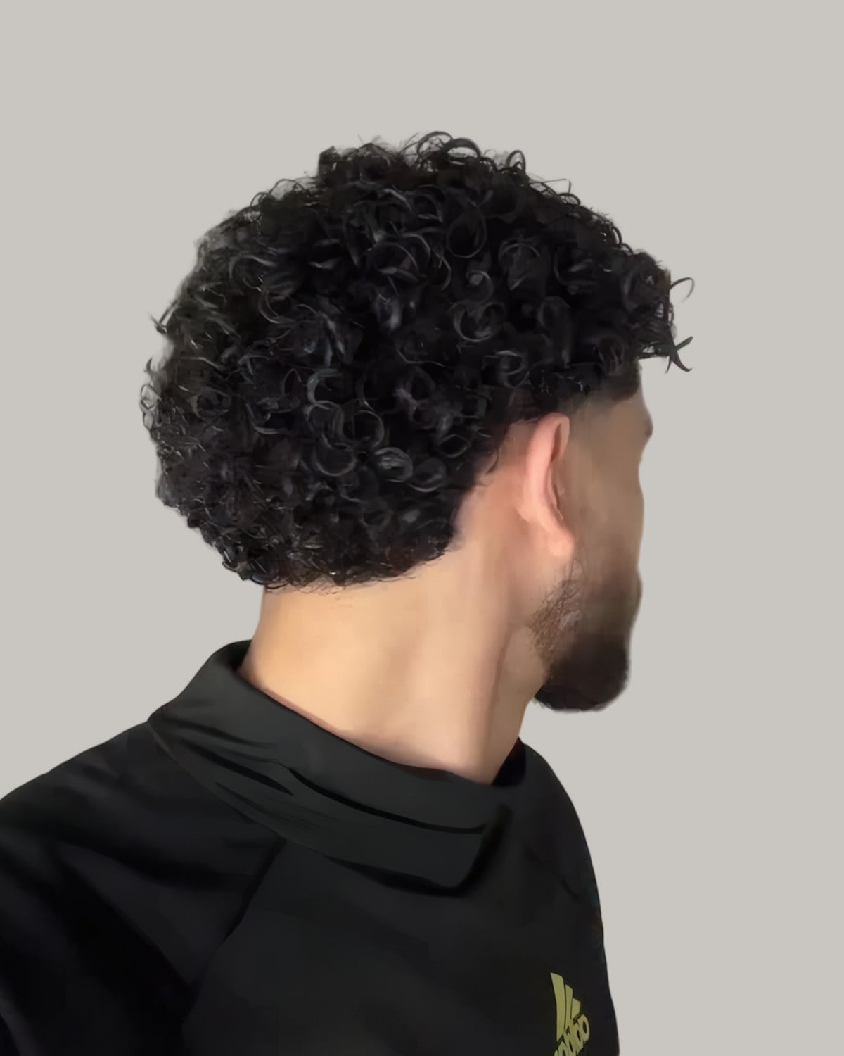 Man with a round mass of tight curls and a faded neckline, seen from behind at an angle