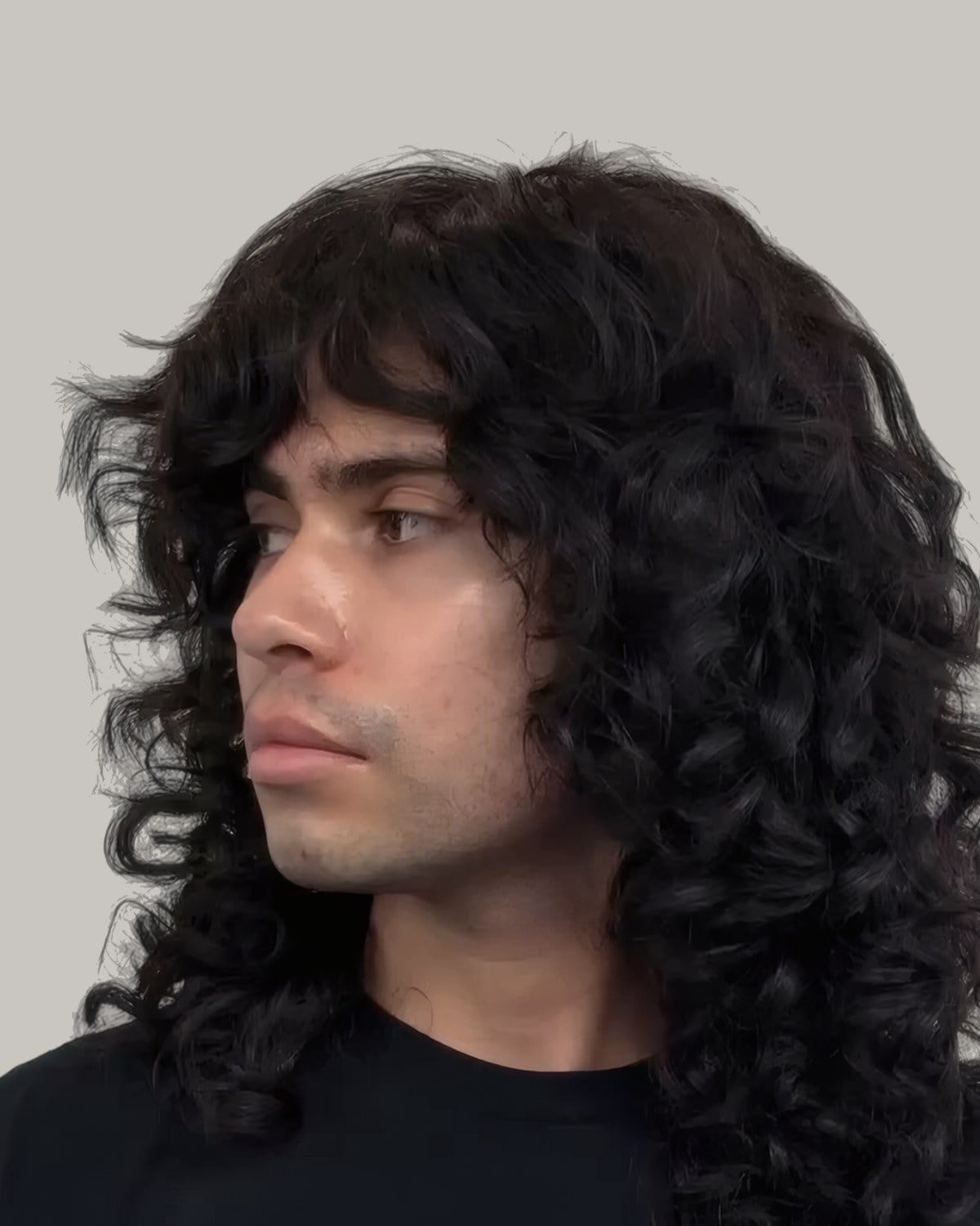 Man with long dark curls and a fringe, seen in profile
