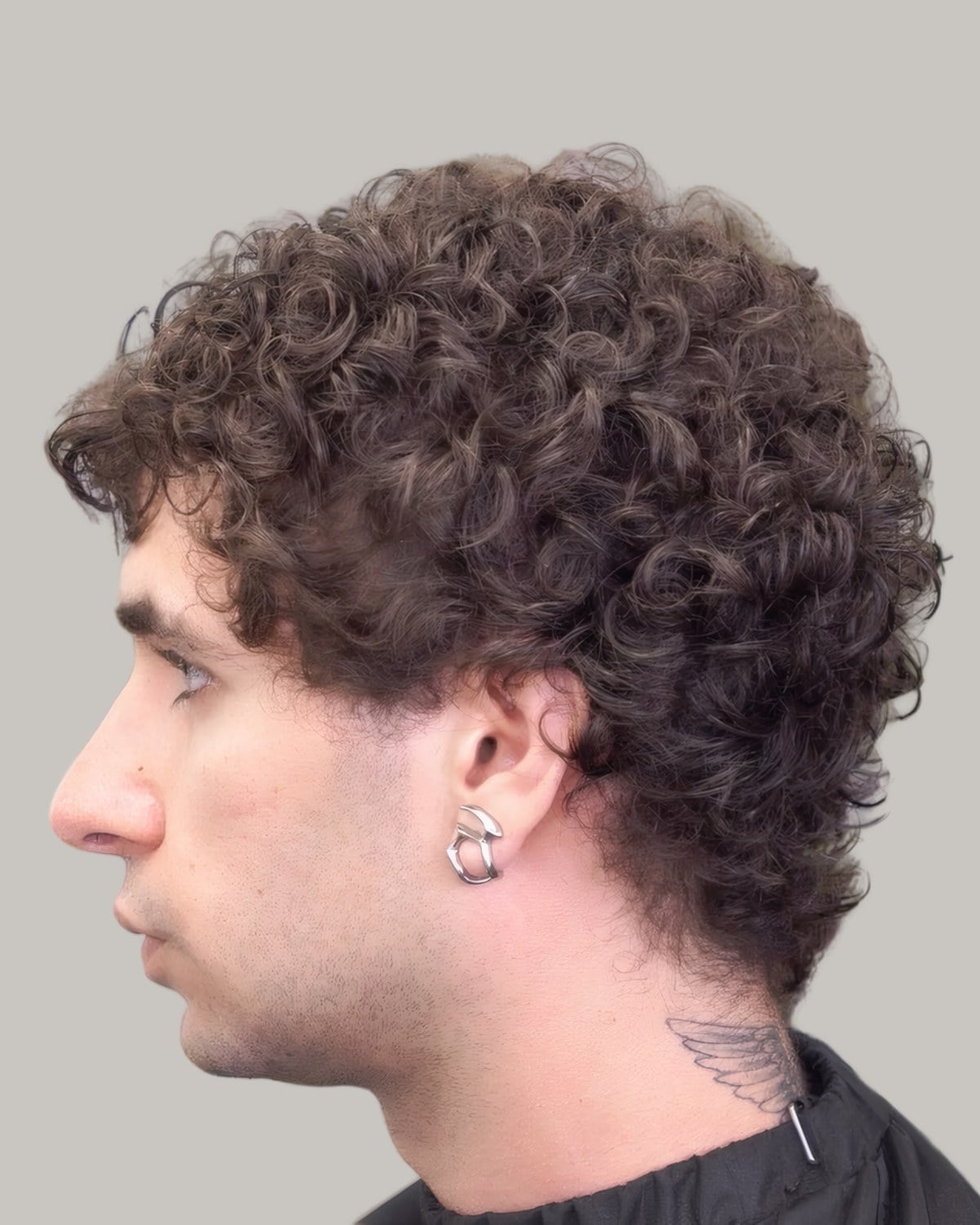 Man with dense dark curls and a short taper at the neck, seen in profile