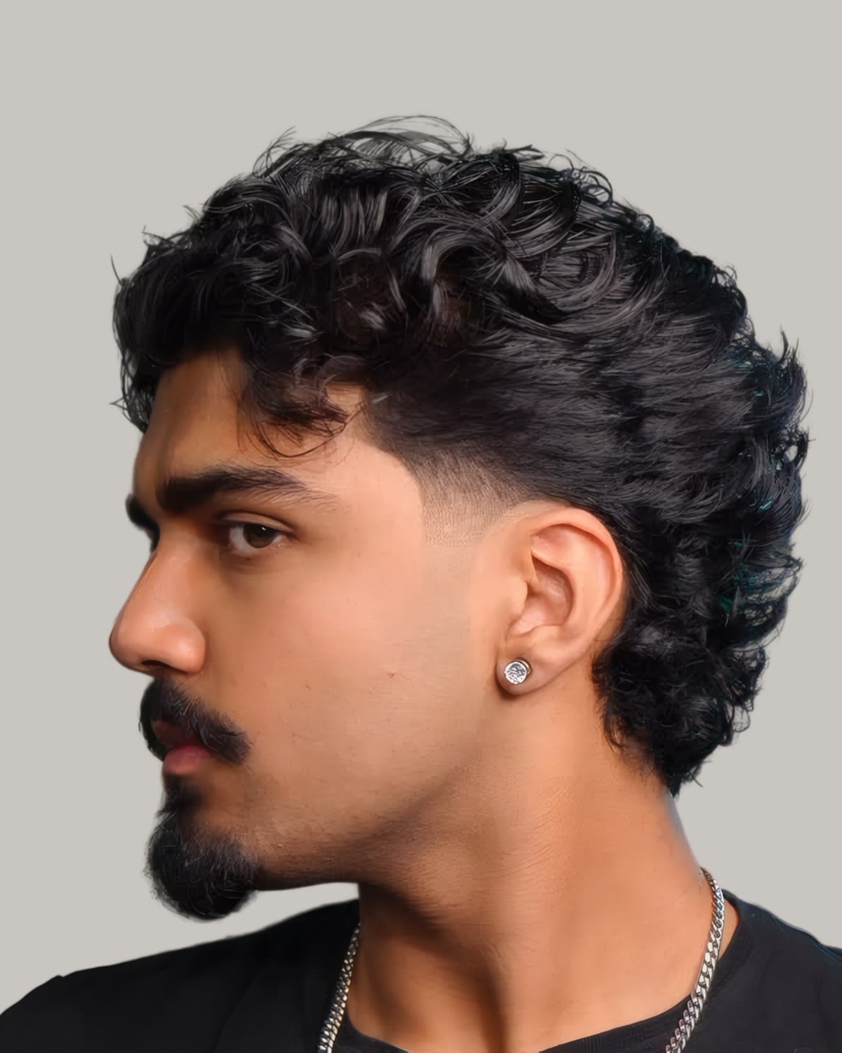 Man with loose dark curls and a low taper at the temple, seen in profile