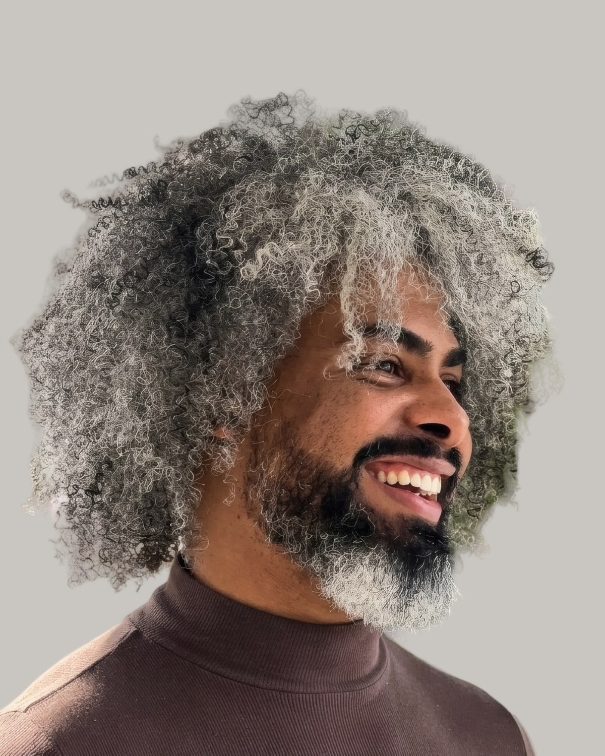 Smiling man with a big mass of grey curls and a beard, seen from the side