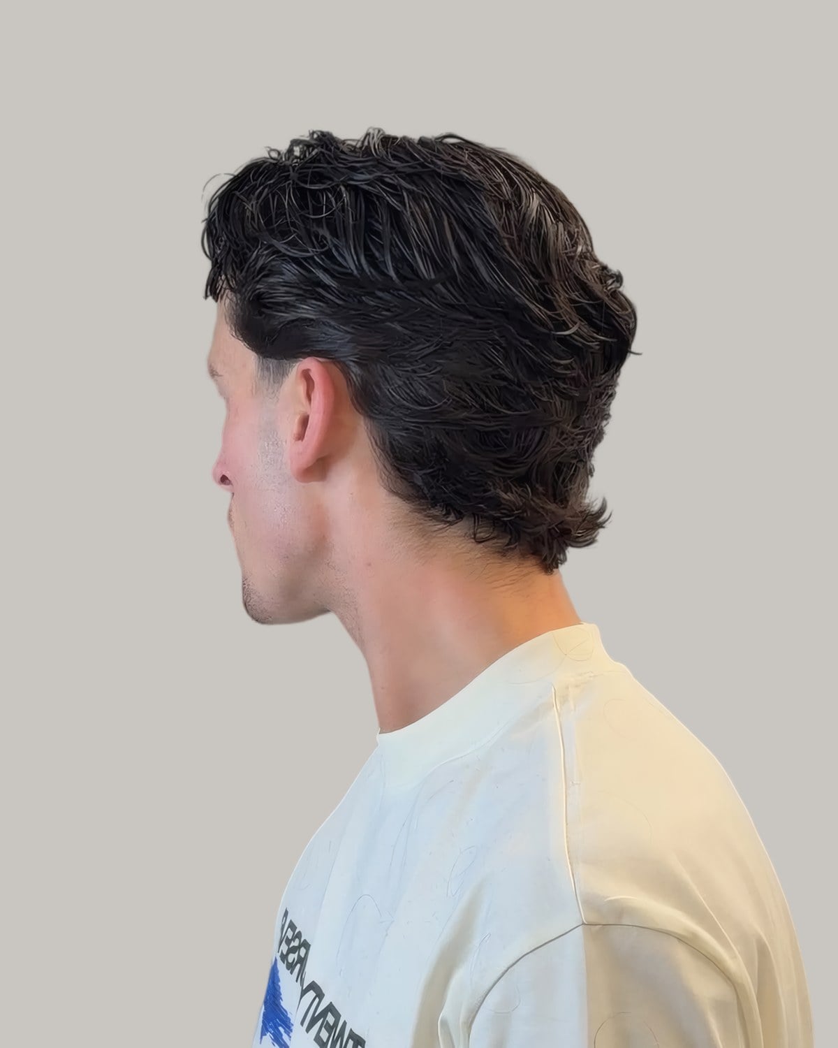 Young man with wavy hair falling to the collar, seen from behind at an angle