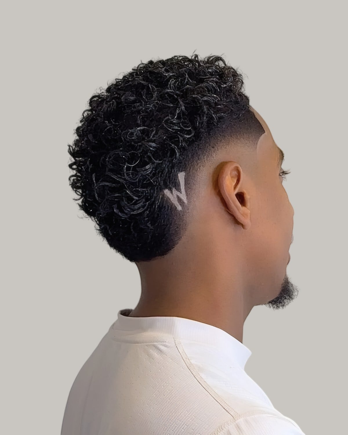 Young man with short tight curls and a low taper, seen from the side at an angle