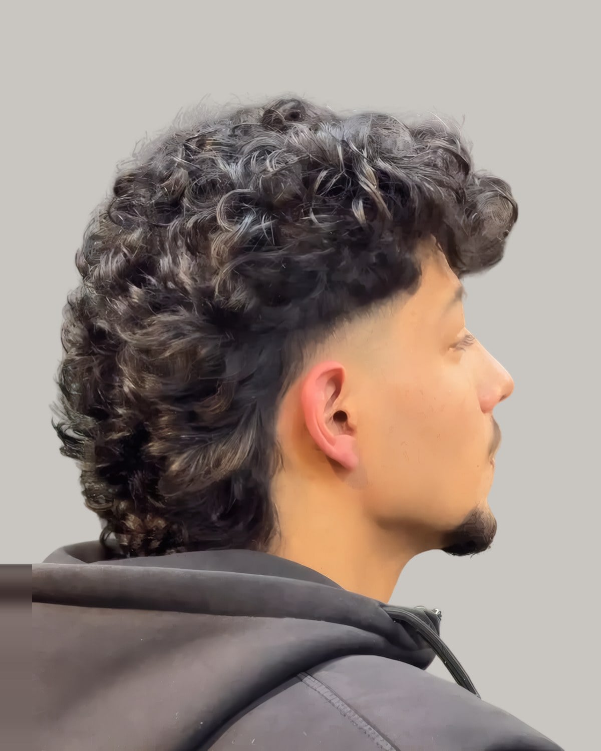 Young man with a curly mullet and a taper, seen in profile