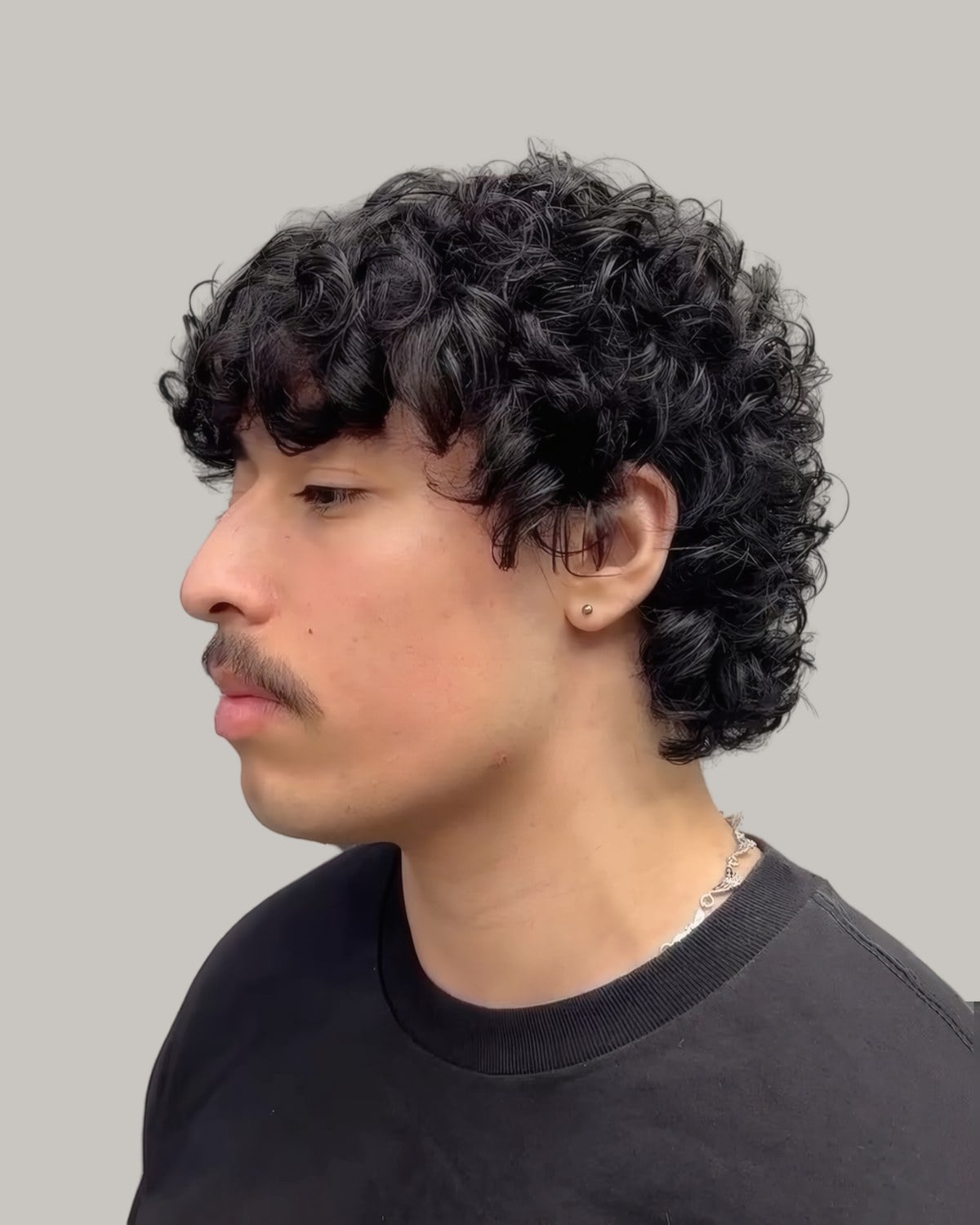 Man with a mustache and curls falling over a low taper, seen from the side