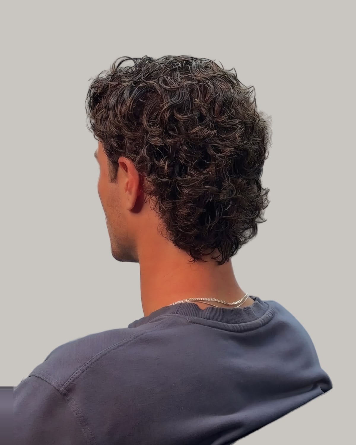 Man with medium curls reaching the collar, seen from behind at an angle