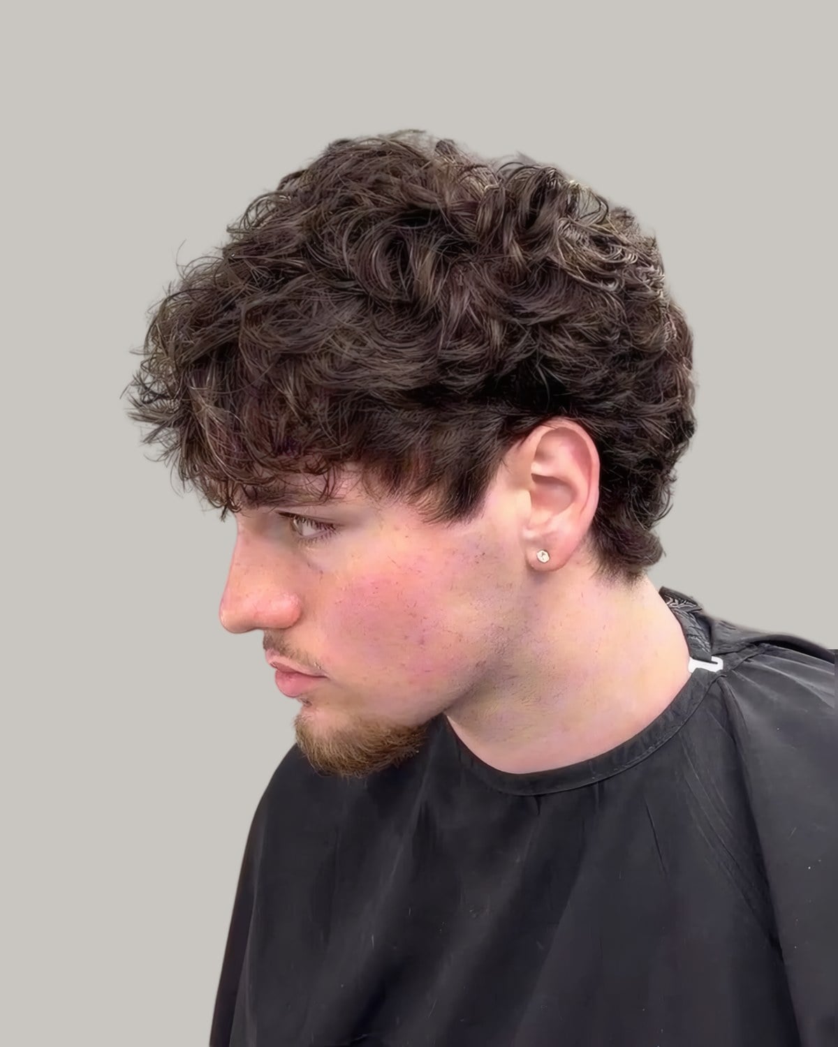 Man with messy dark curls and a taper, seen from the side