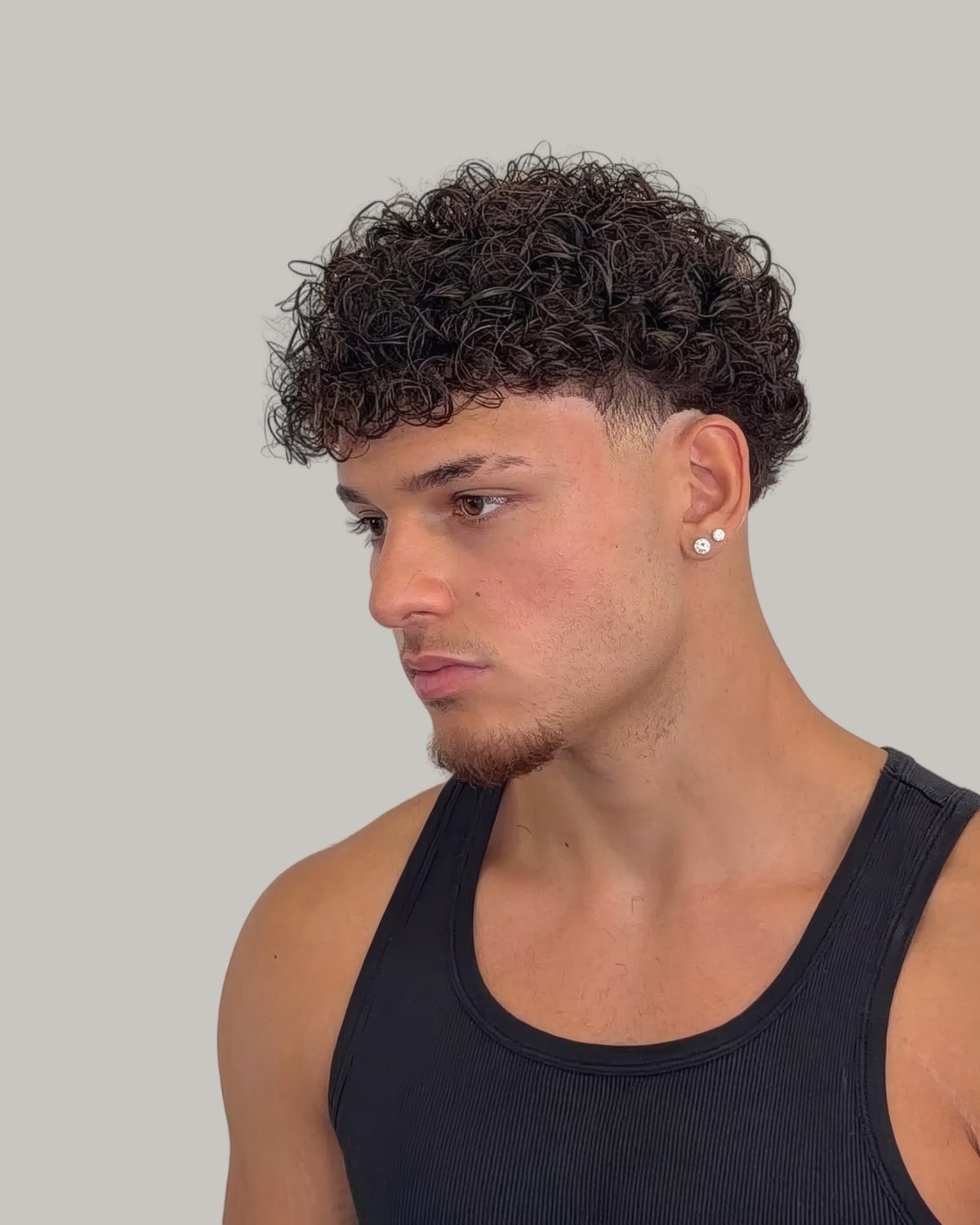 Young man in a tank top with short curls and a fade, seen in profile